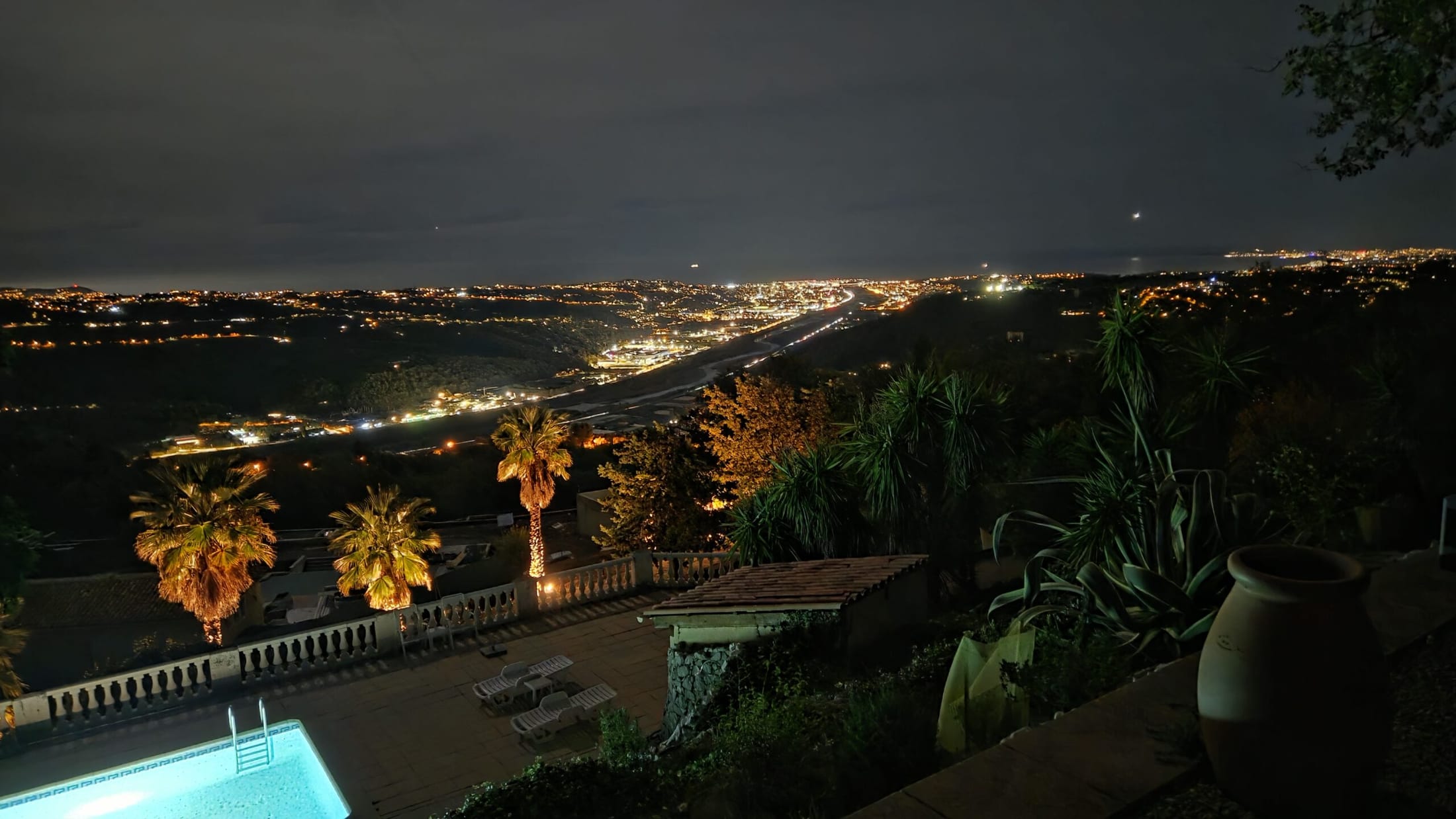 Vue de nuit sur la piscine éclairée et la vallée jusqu’à la côte.